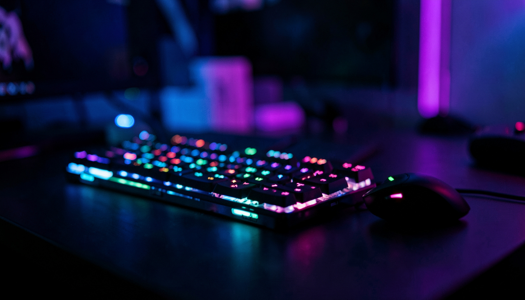 Dark gaming setup with glowing RGB keyboard and mouse on a desk, deep blue and purple ambient lighting, immersive mood